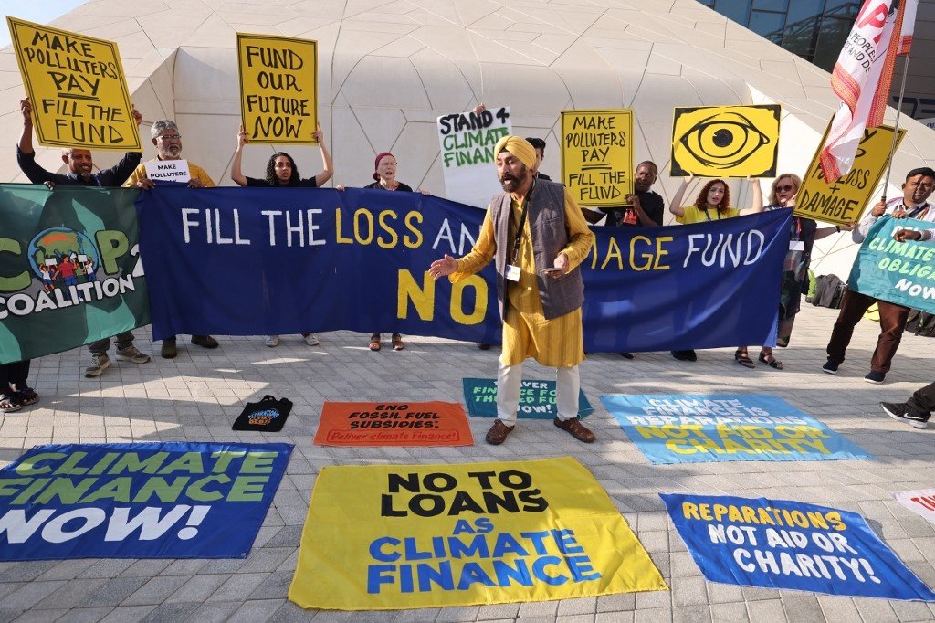 活动人士当地时间周一在COP28场外举起标语牌并高呼口号，呼吁世界上最大的二氧化碳排放国填补“损失与损害”基金，以支持最容易受到气候变化影响国家的适应与发展。（图取自法新社）