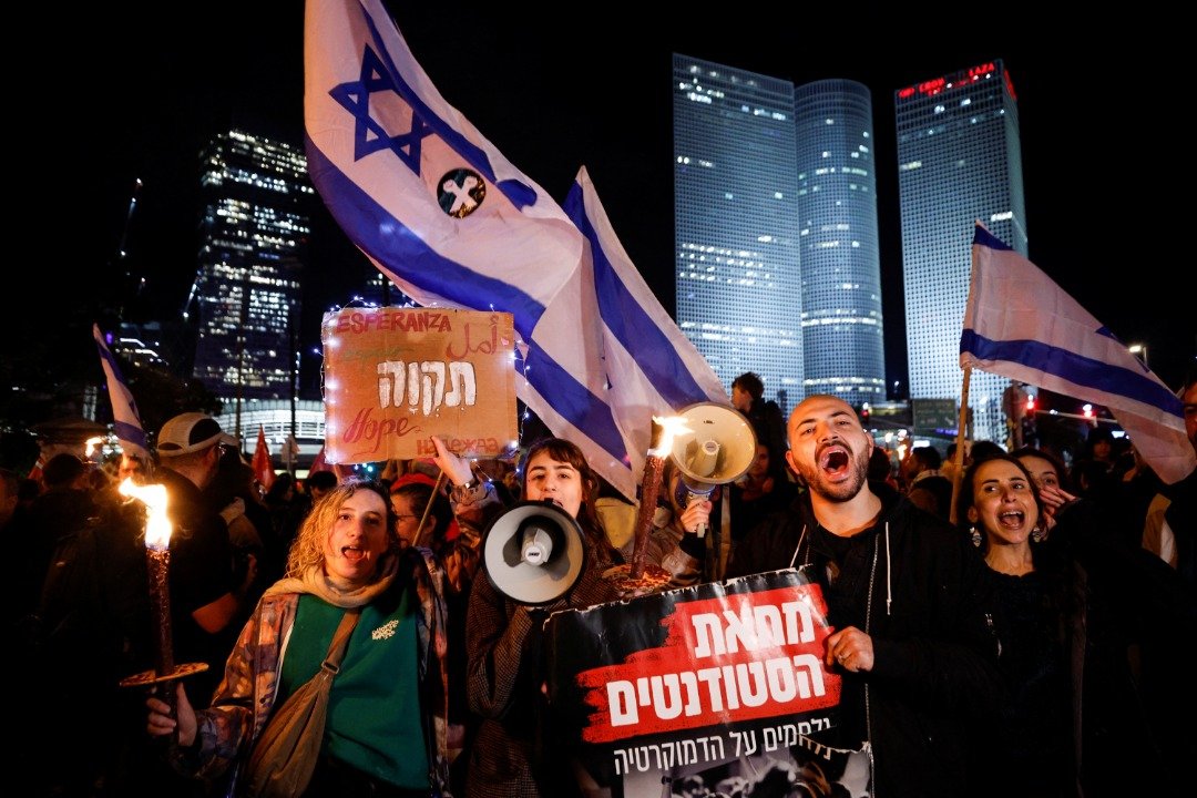 民众挥舞著以色列国旗、手持希伯来语抗议牌，反对新的右翼联合政府改革司法机构的计划。（图取自路透社）