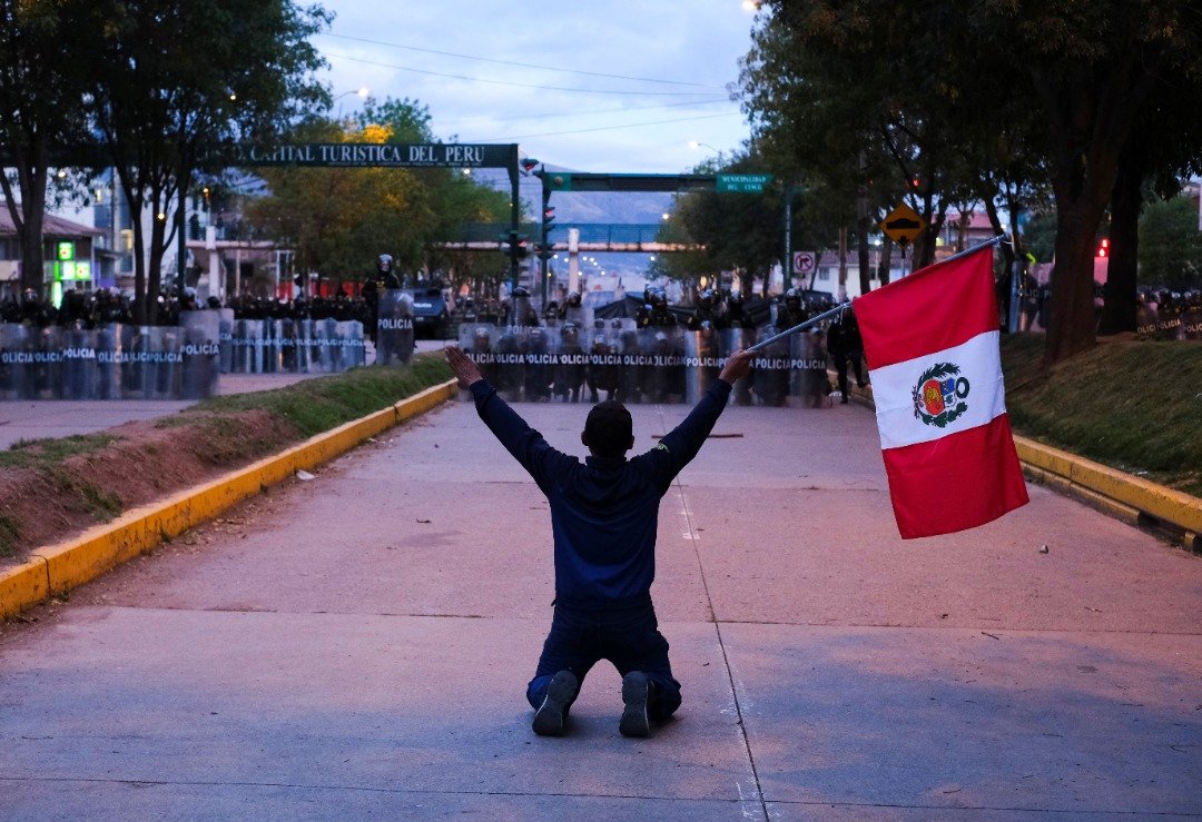一名示威者跪地手持秘鲁国旗，要求总统博卢阿尔特下台。在他前方的是装备完善的防暴警察。（路透社）