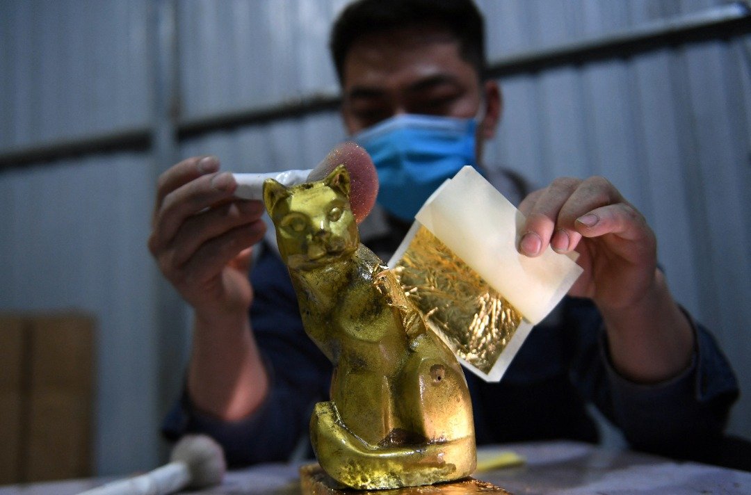 图为去年12月15日，一名男子在河内一家工厂为一座猫雕像镀金，以在来临的农历新年推出市场。（图取自法新社）