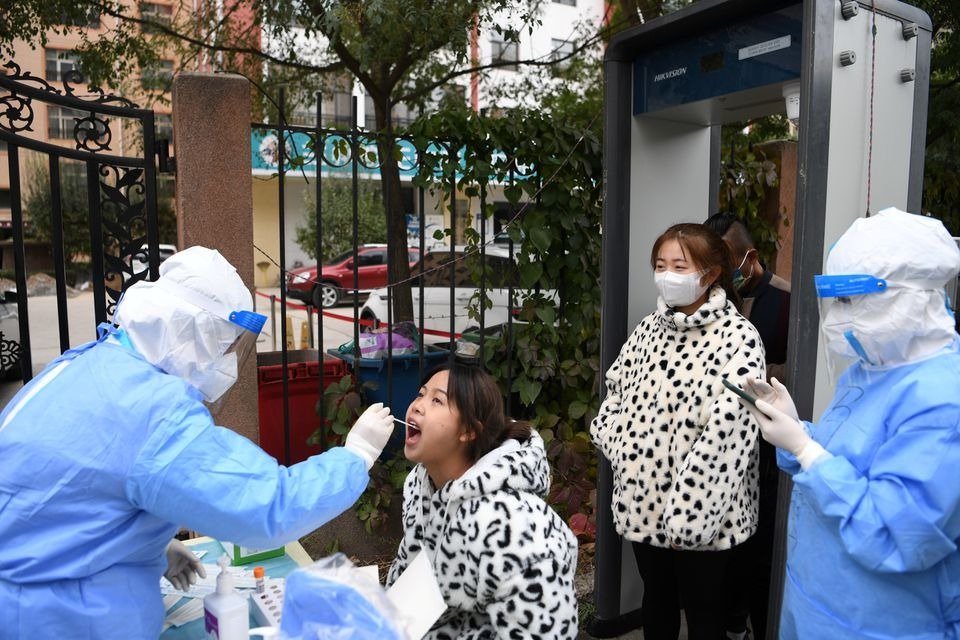 2021年10月20日在中国甘肃省兰州市城关区，一名身穿防护服的医务人员在一个免费核酸检测点从居民身上采集拭子。（图取自路透社档案照）