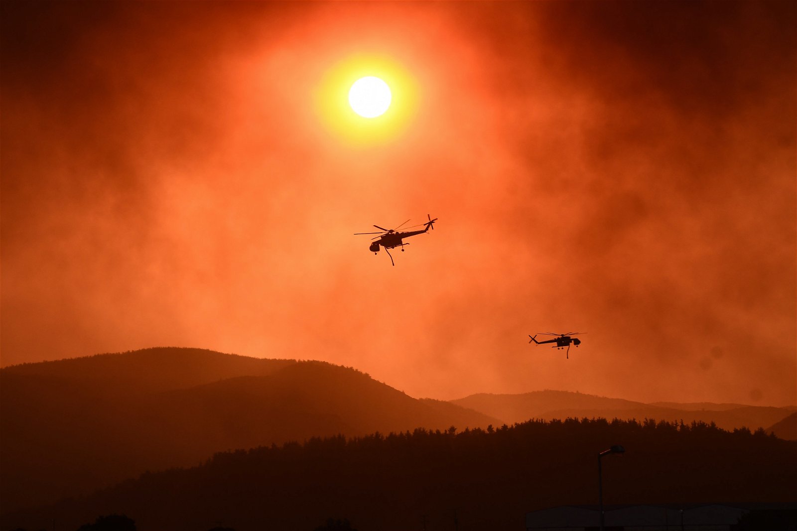 野火肆虐希腊北部的森林，救援直升机在被染红的上空飞过。（图取自法新社）