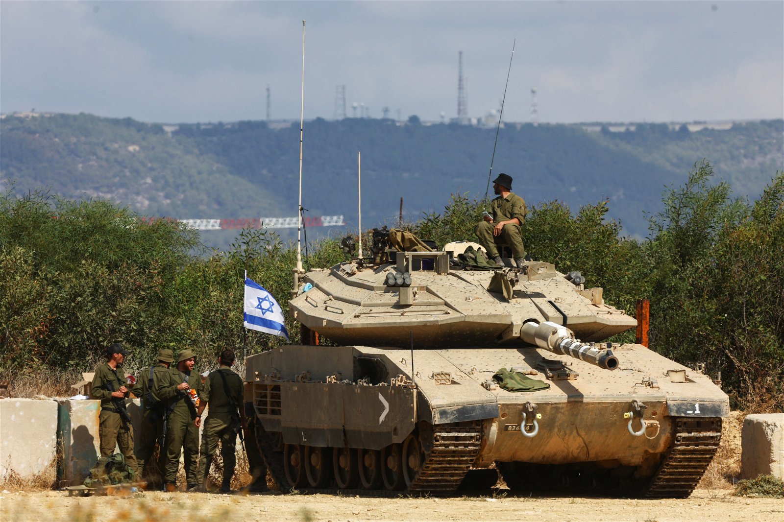 以色列士兵站周一在与黎巴嫩边境的以色列北部附近，在一辆坦克车旁就位。（图取自路透社）