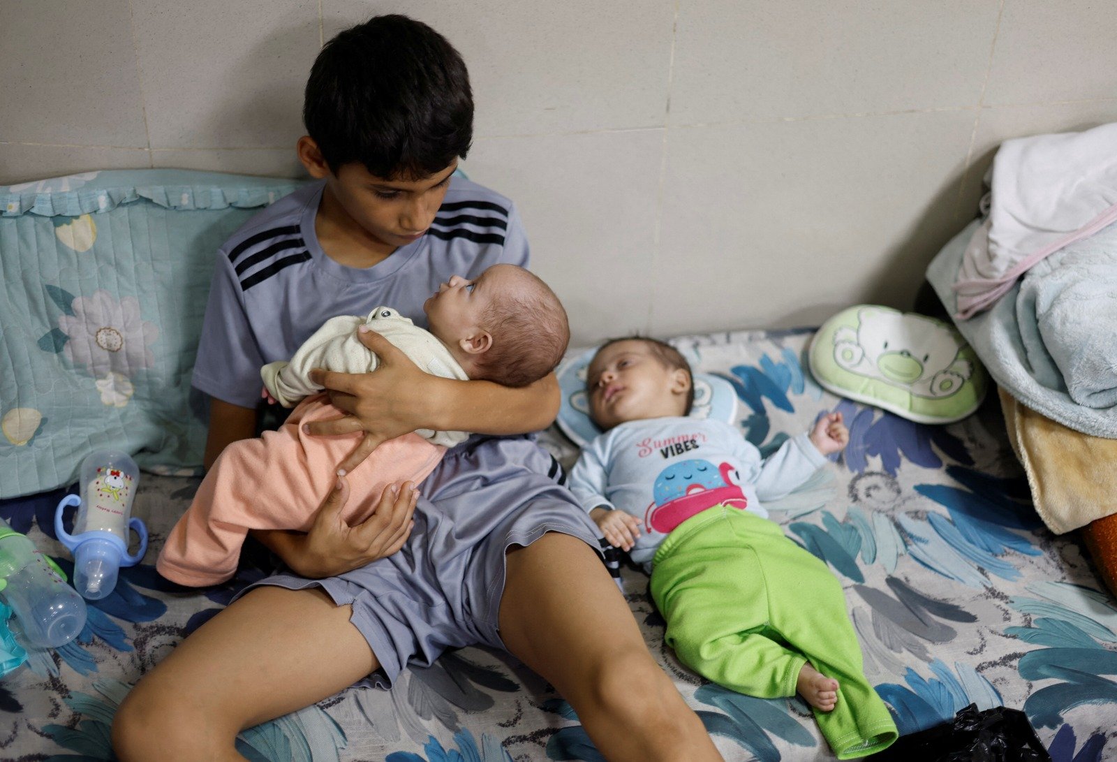 在加沙地带南部汗尤尼斯的纳赛尔医院，一名因躲避以军空袭而与家人流离失所的巴勒斯坦男孩周日在医院避难时，照顾他的双胞胎弟弟。（图取路透社）