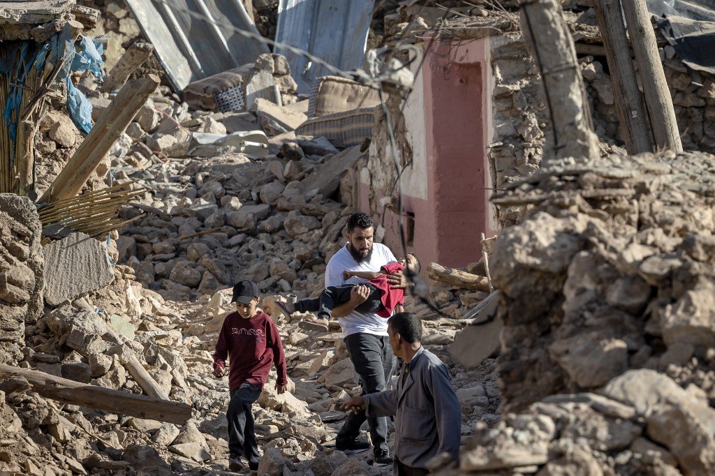 在马拉喀什市西南部的塔菲加特山村，村民们走过因强震变成一片废墟的建筑瓦砾。（图取自法新社）