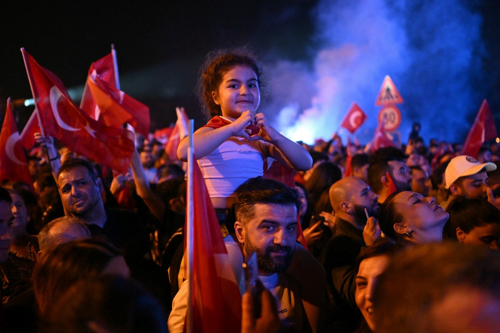 在伊斯坦布尔，共和人民党 (CHP) 支持者周日晚在主要市政大楼外庆祝，一名骑在父亲肩头上的小女孩比著爱心手势。（图取自法新社）