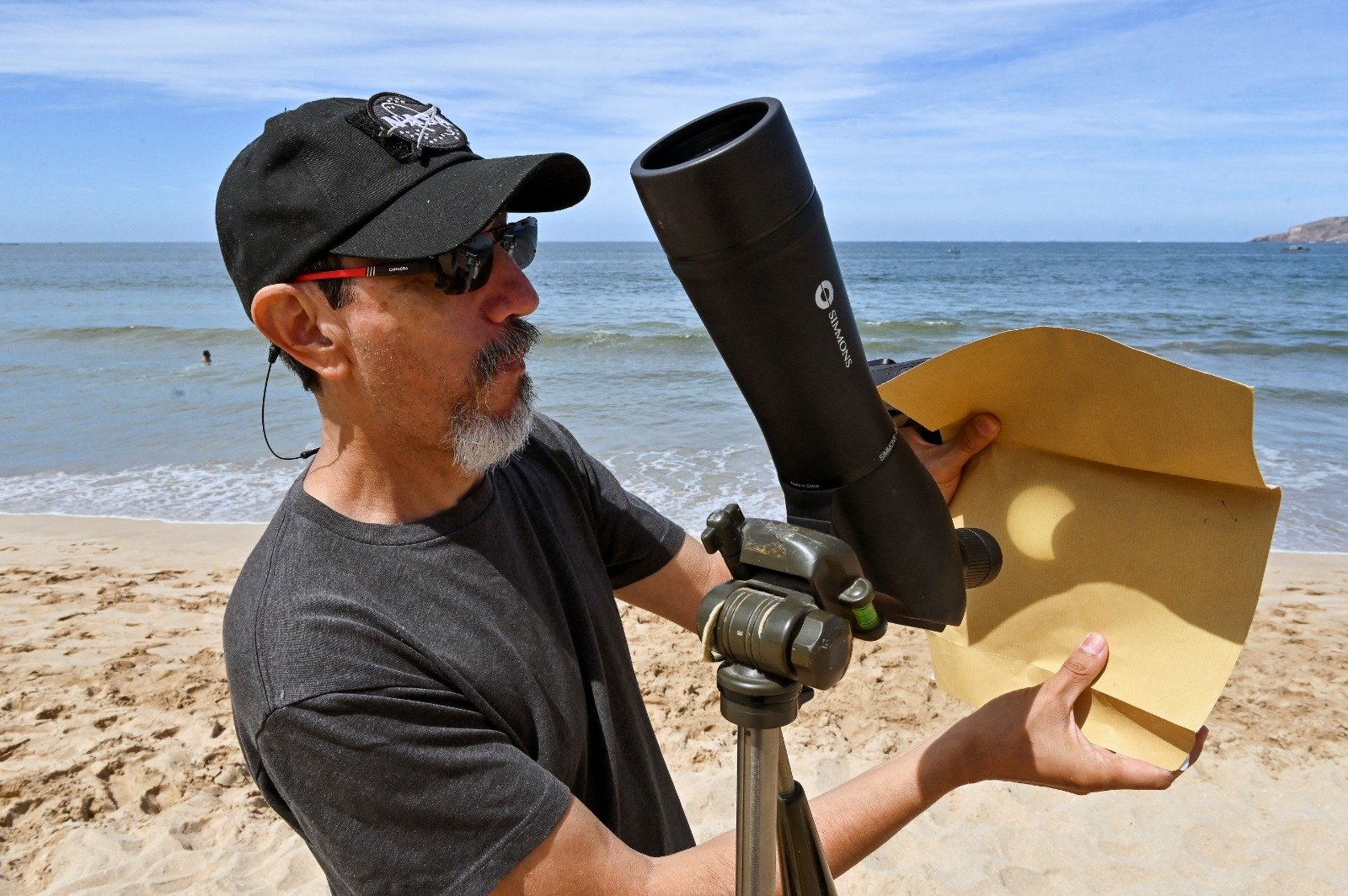 在墨西哥锡那罗亚马萨特兰的海滩上，日全食发生前，一名男子用单筒望远镜反射太阳的阴影。（图取自法新社）