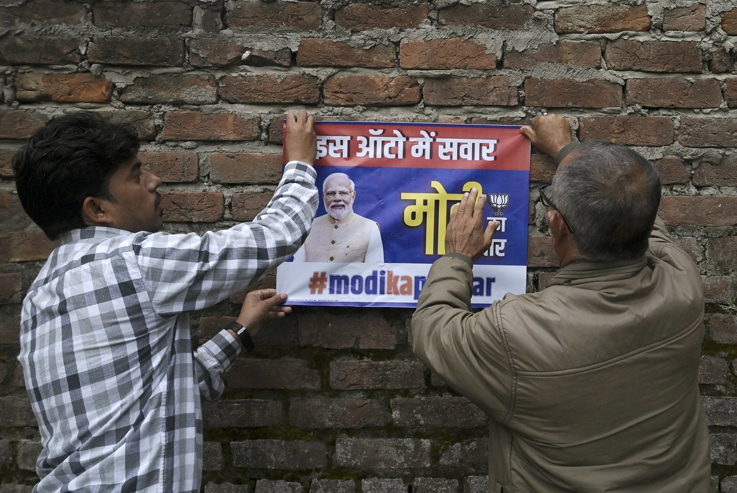 执政党印度人民党的活动人士，周五在查谟市一个投票站附近的墙上，张贴一张印有总理莫迪肖像的海报。（图取自法新社）