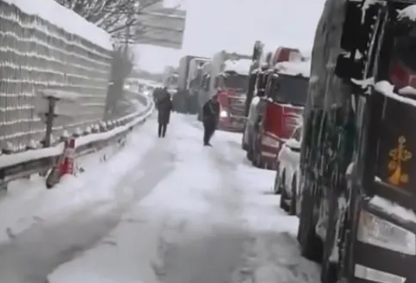 上坡路段因结冰，两辆大货车并排停放在路中间，导致高速公路交通一动不动。