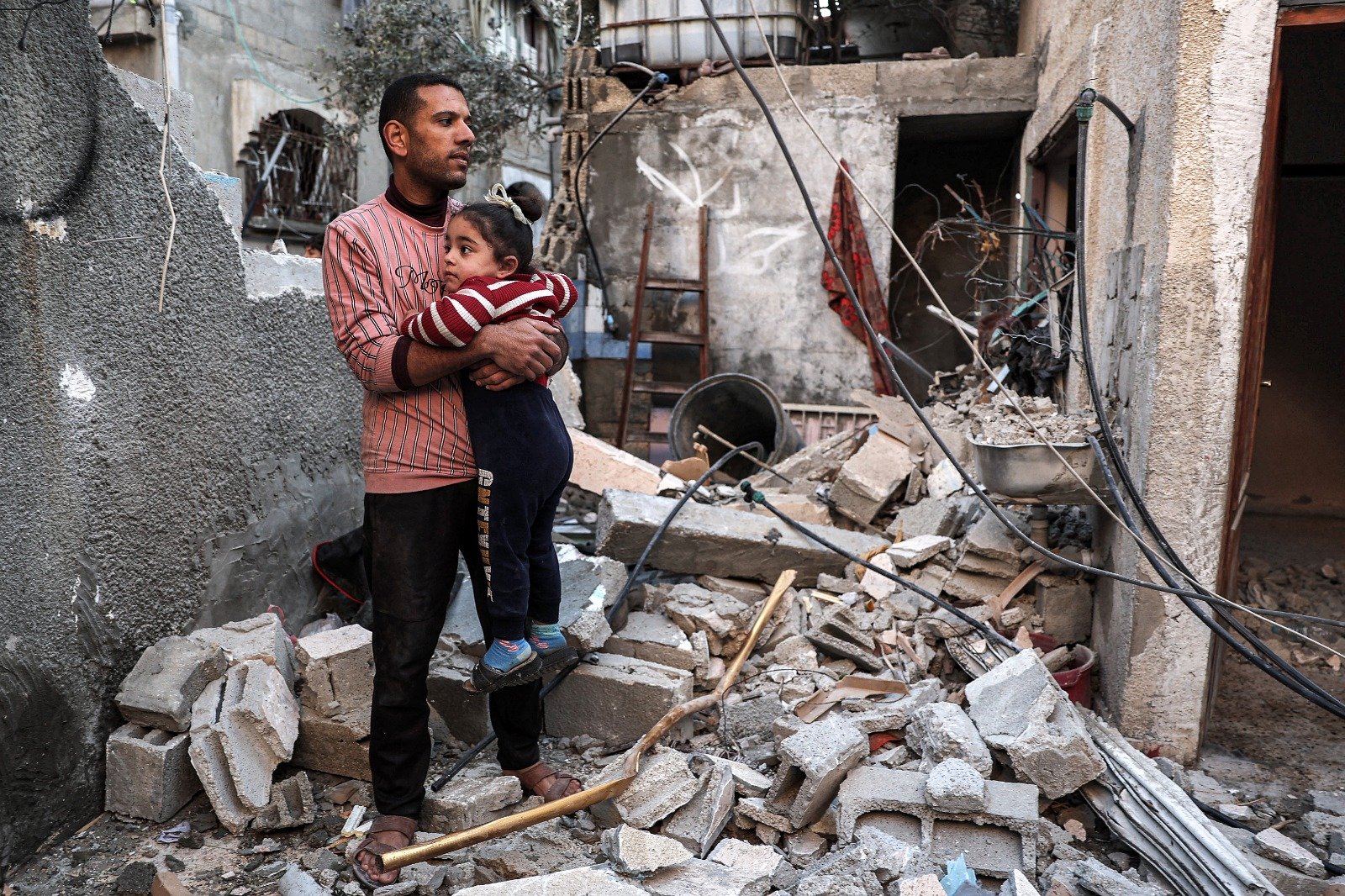 以色列和哈马斯之间的冲突进入第5个月，一名巴勒斯坦男子周四抱著一名小女孩，站在以色列对加沙地带南部拉法轰炸摧毁的公寓废墟中。（图取自法新社）