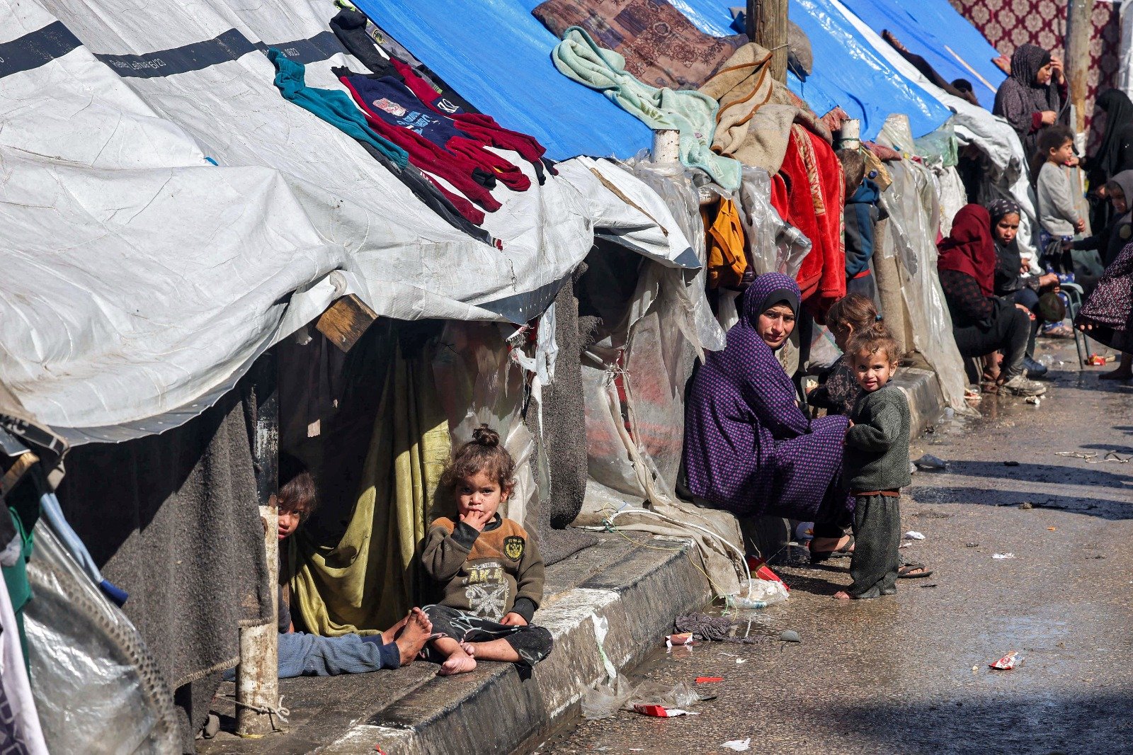 在加沙地带南部拉法，一名妇女和儿童周四坐在庇护流离失所巴勒斯坦人的帐篷外。目前，有超过100万巴勒斯坦人在拉法寻求庇护。（图取自法新社）