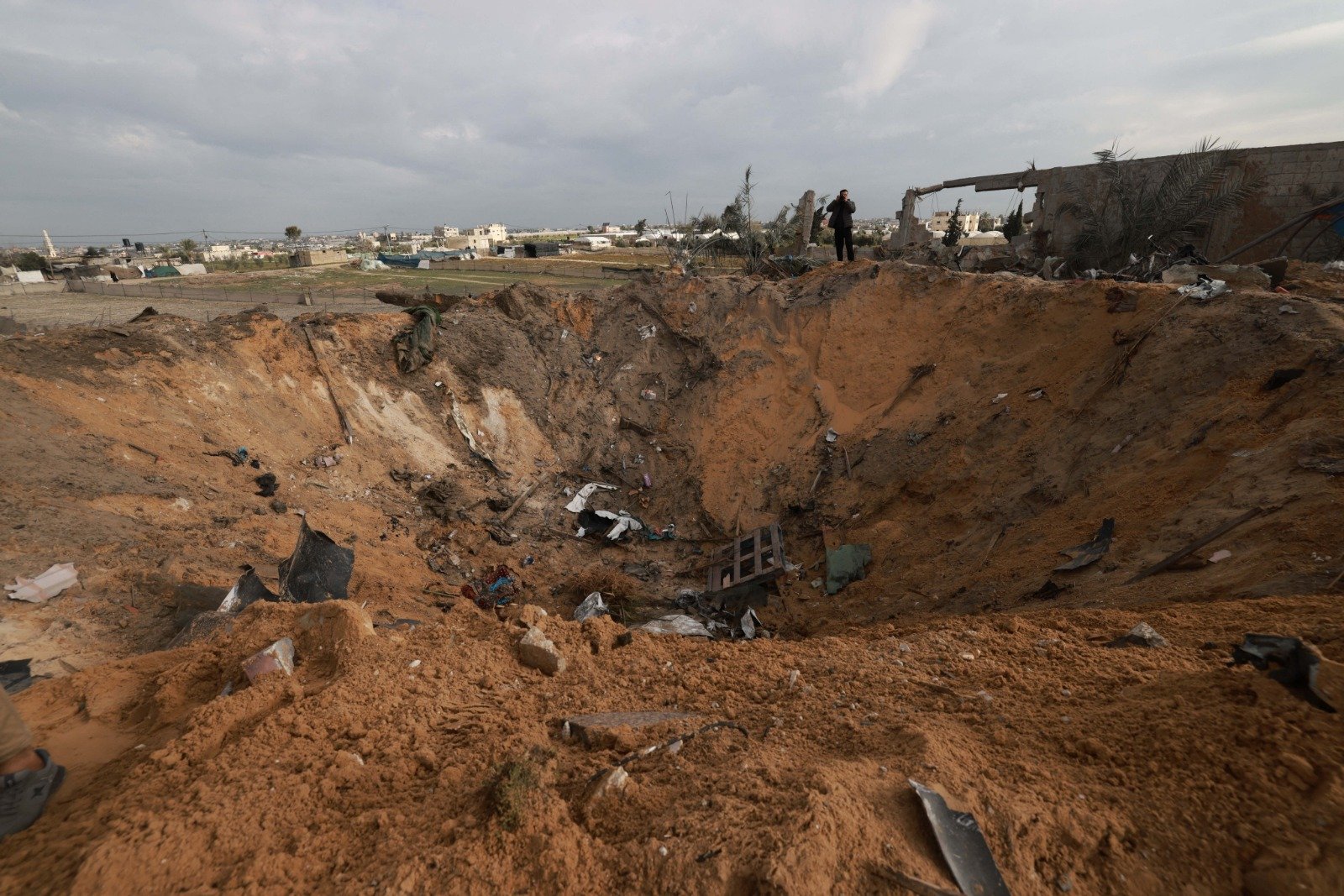 以色列和哈马斯的战斗仍在持续，以军连夜空袭加沙地带南部边境城市，一名巴勒斯坦人周日站在拉法的一个巨大弹坑旁。（图取自法新社）