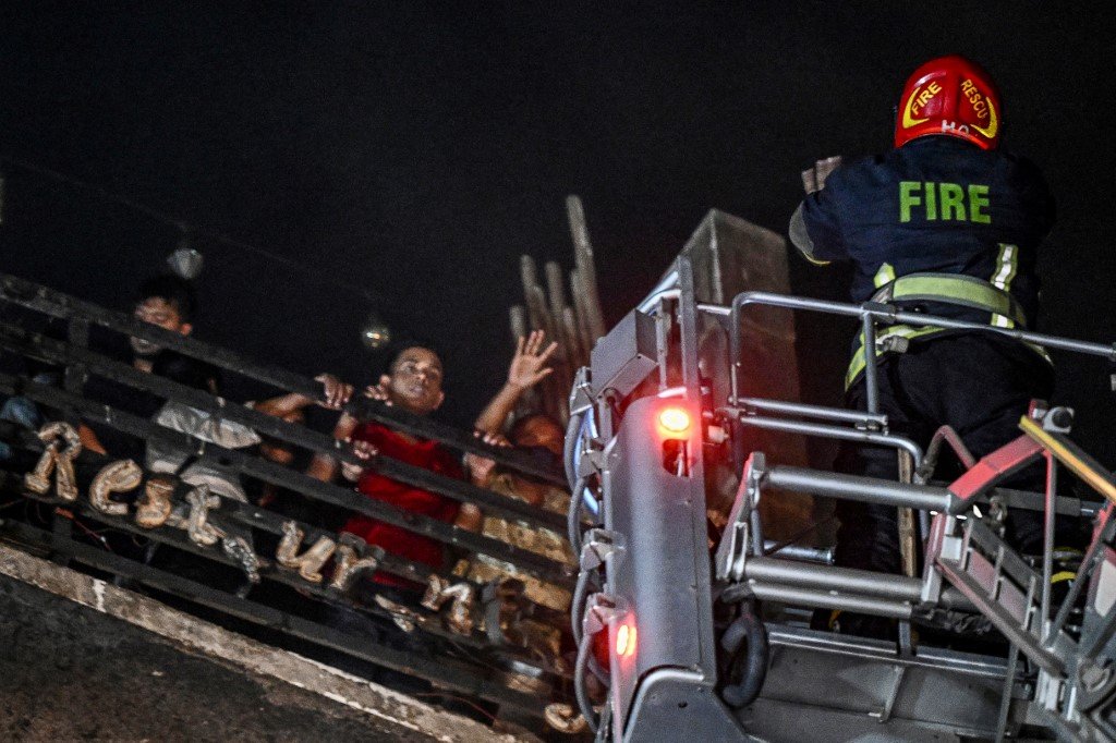 被困在屋顶上的人大声呼救，消队员出动消防梯救出受困者。（图取自法新社）