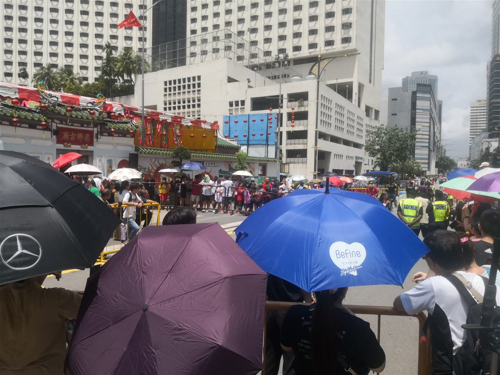 数千信众撑著雨伞，在烈日下聚集在古庙前，等待五尊神明回銮。