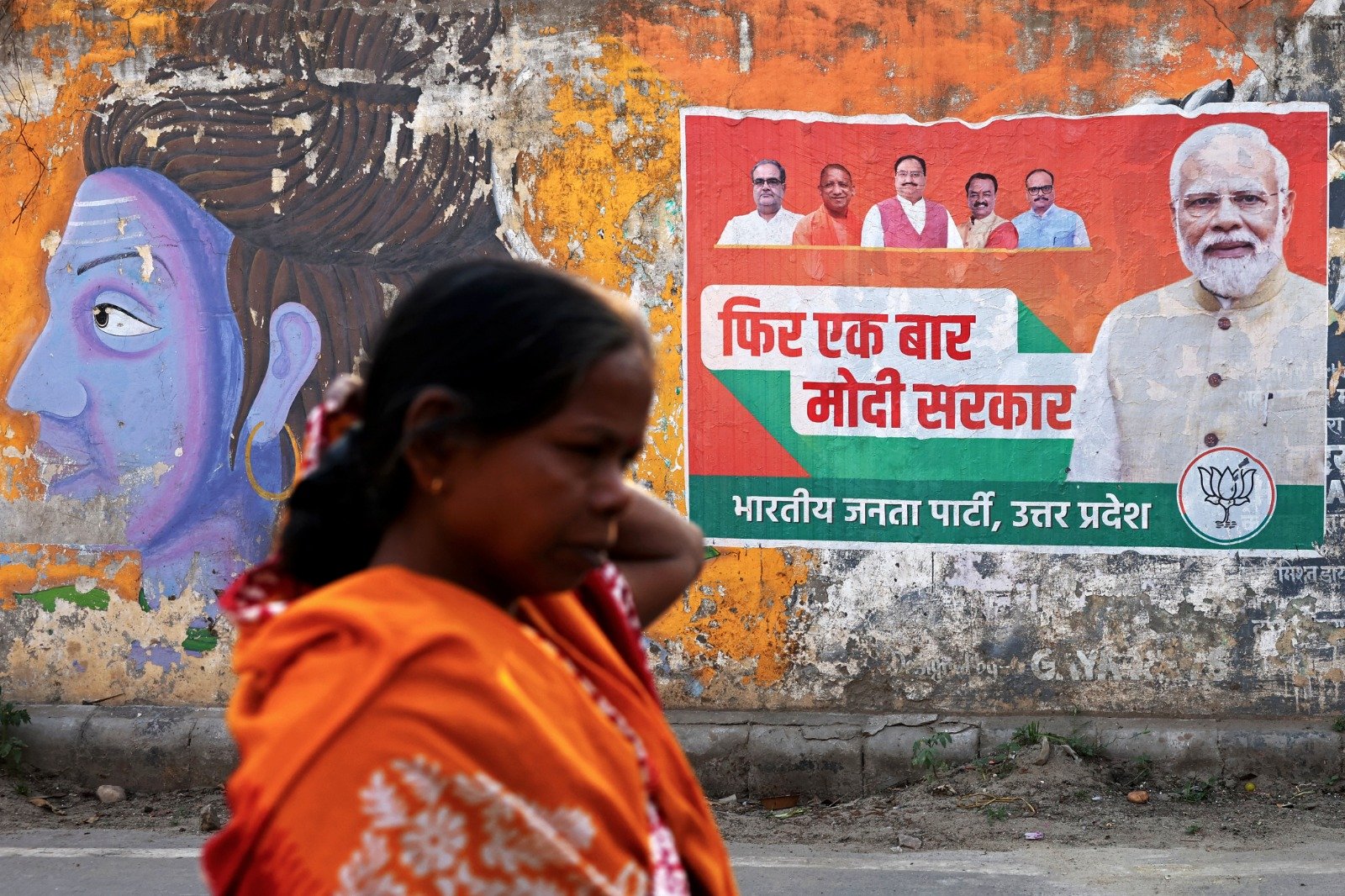 印度即将在下月举行全国大选，一名妇女周日在瓦拉纳西的一条街道上走过执政印度人民党(BJP) 的竞选海报，海报上印著该党领导人和印度总理莫迪的照片（右）。（图取自法新社）