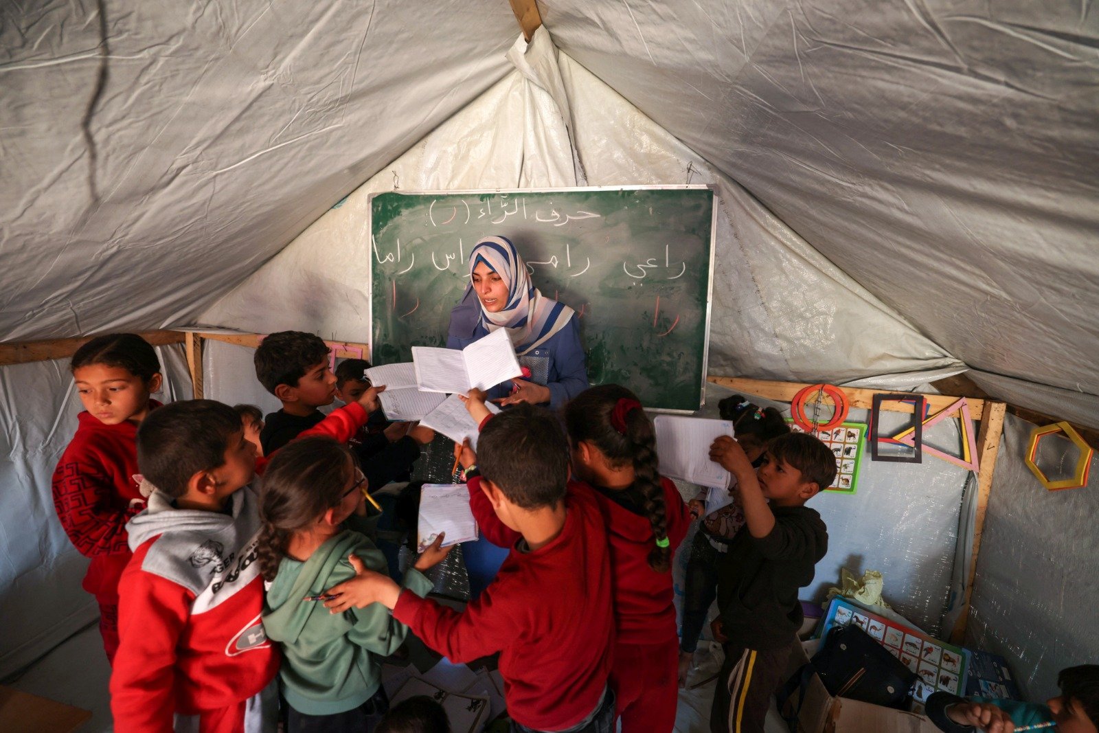 拉法是加沙地带唯一仅存还未遭以军地面进攻的区域，当地挤满了150万巴勒斯坦平民。外界忧心，以军一旦发动地面攻势将造成更严重的人道主义灾难。图为在流离失所的巴勒斯坦人营地中，孩子们在临时教室里交出笔记本。（图取自法新社）