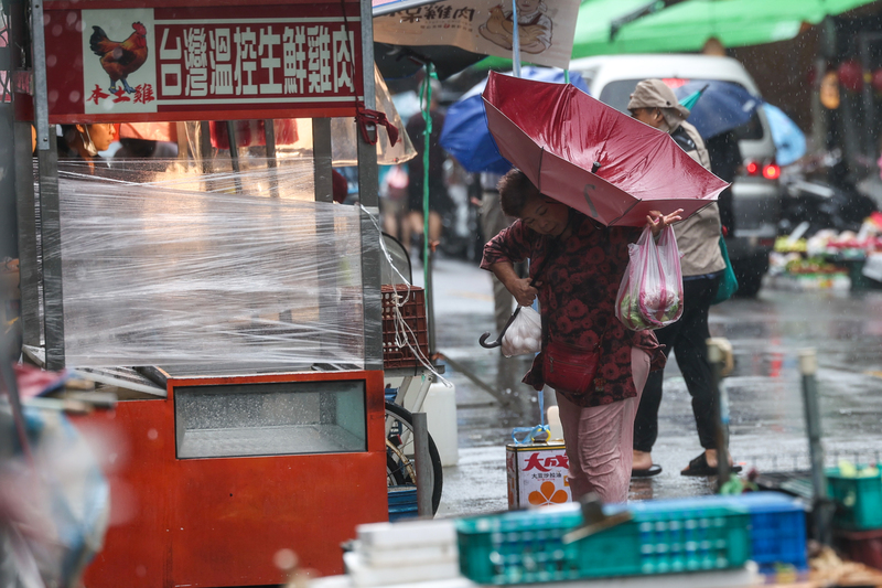 民众周五在台湾台北市滨江市场采购时，雨伞被大风吹翻。（图取自台湾中央社）