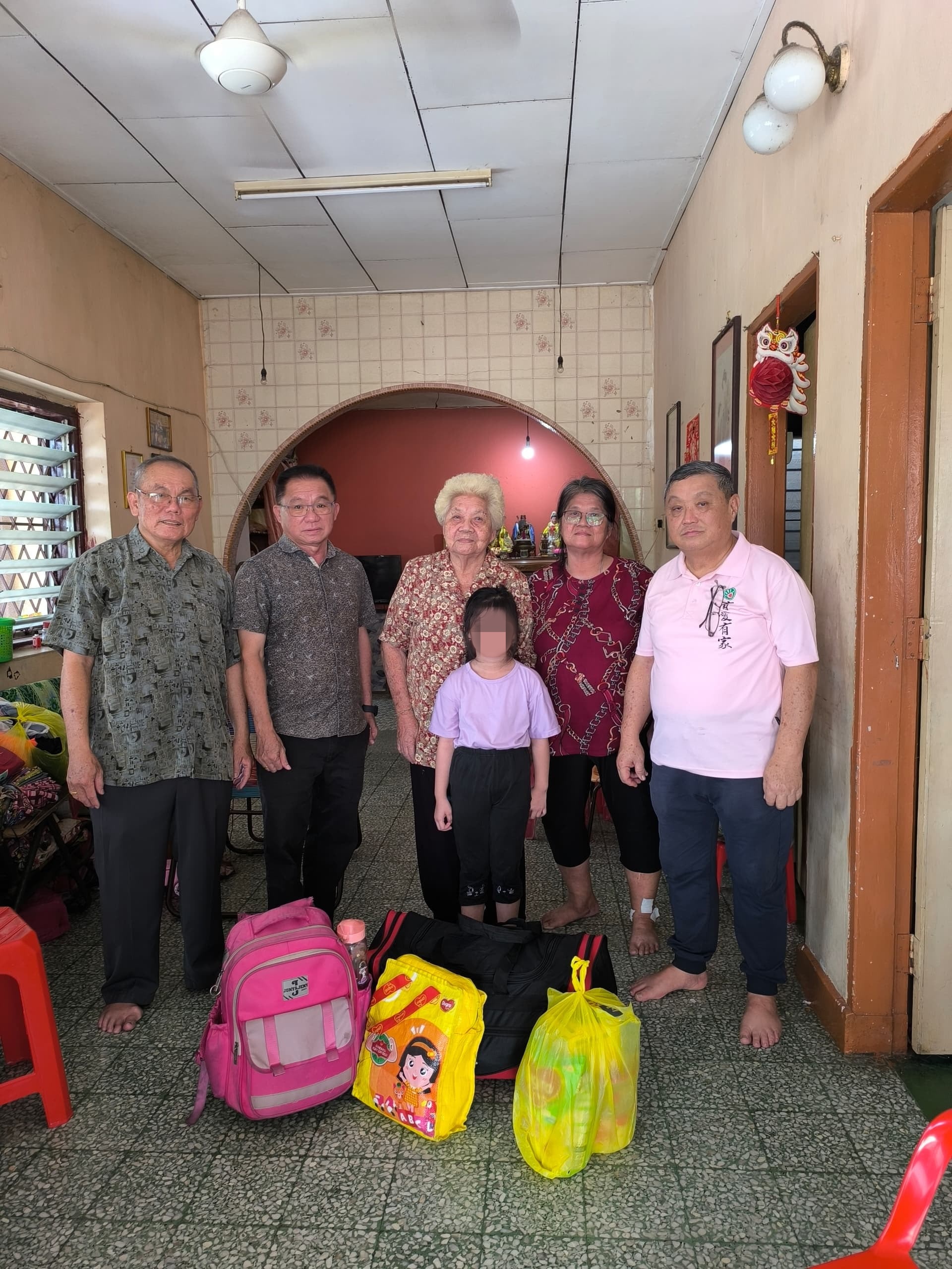 安顺杰护幼之家代表前往接领孩子，与祖孙三人合影。地上已收拾好的书包与行李，准备带往护幼之家。左起为纪曜贤、江顺进、蔡巧清、纪金花及陈明华。