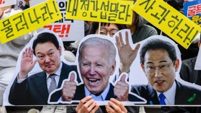 在日本首相岸田文雄访韩的前一天，在首尔的集会上有反对的民众举著有韩国总统尹锡悦（左起）、美国总统拜登与岸田的肖像。（图取法新社）
