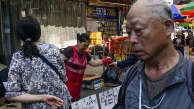8月4日在韩国首尔的市场摊位上，一名小贩出售一袋鱼。（图取自法新社）