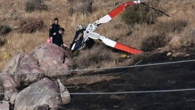 调查人员于当地时间周一加利福尼亚州卡巴松烧毁的山坡上，绕著一架坠毁直升机的旋翼叶片勘察。（图取自法新社）