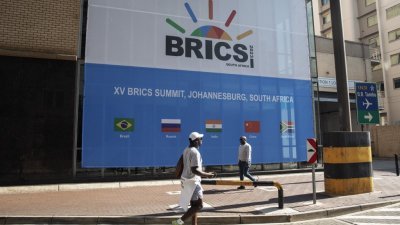 南非约翰内斯堡桑顿的桑顿会议中心，人们走过2023年金砖国家峰会会场外的横幅。为期3天的金砖峰会于周二起，在约翰内斯堡举行。（图取自法新社）