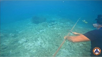 周一发布的视频截图显示，一名菲律宾海岸警卫队人员切断连接黄岩岛附近安装的浮动屏障的绳索。（图取自菲律宾海岸警卫队/法新社）
