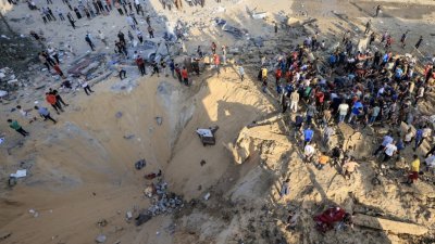 在加沙南部城市汗尤尼斯，当地巴勒斯坦人周一围绕在以色列空袭爆炸造成的弹坑旁。（图取自法新社）
