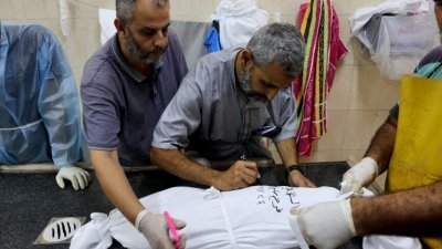 在加沙地带南部拉法的纳贾尔医院，一名巴勒斯坦医生周二在一名包裹著儿童尸体的白布上写下了“法拉.阿布.沙巴布”的名字。（图取自法新社）