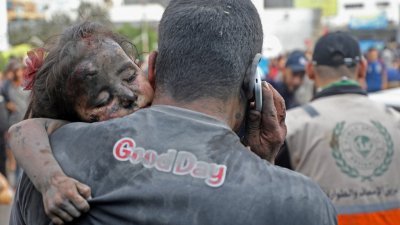 以军在周日持续空袭加沙地带，一名满身灰尘的巴勒斯坦男子抱著一名受伤的小女孩进入加沙城的希法医院。（图取自法新社）