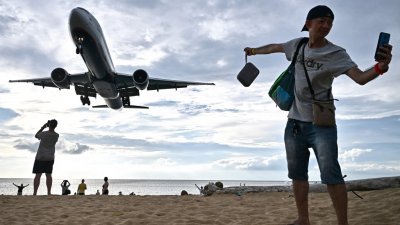 飞机降落在泰国南部普吉岛的普吉国际机场，一名游客在迈考海滩上自拍。（图取自法新社）