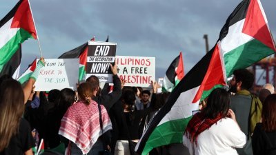 澳洲巴勒斯坦社区成员周二在悉尼博塔尼港码头举行抗议活动时，举著旗帜和标语牌。在周三，警方宣布他们对抗议活动中的23人提出指控，声称他们试图封锁通往港口设施的道路。（图取自法新社）
