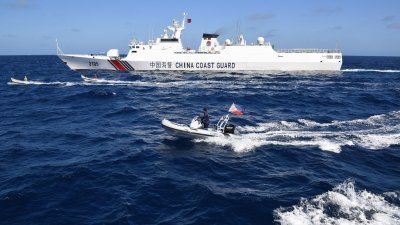 2月16日拍摄的照片显示，乘坐木船的菲律宾渔民（左中和左2）以及乘坐刚性船体充气船的菲律宾渔业和水产资源人员（前中），驶过附近的一艘中国海警船。（图取自法新社）