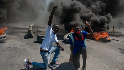 周二在海地首都太子港，在总理亨利辞职后举行的示威活动中，街道上的轮胎被烧毁，抗议者高举紧握的拳头。（图取自法新社）