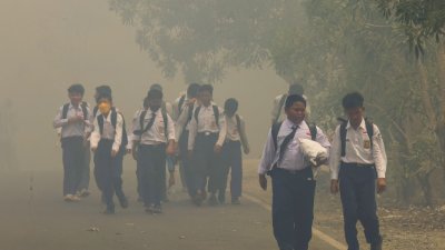 周三在南加里曼丹省班贾尔巴鲁县的德加尔阿鲁姆，学生们走在烟雾弥漫的道路上，大规模的森林和土地火灾使该地区笼罩在浓厚的烟雾之中。（图取自法新社）
