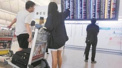 “天鸽”强台风扑向香港、澳门等地，450班来往香港的航班取消，大马主要机场飞往港澳及广东的班机也受影响。图为乘客在香港国际机场查看班机情况。