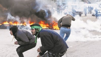 特朗普宣布承认以色列定都耶路撒冷后，巴勒斯坦人在加沙 及西岸各地发起示威。图为靠近雷马拉的一个犹太人定居点， 示威的巴勒斯坦人弯腰躲避以色列军发射的催泪弹。