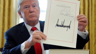 美国总统特朗普周五在白宫椭圆形办公室，签署价值1兆5000万美元税收改革计划后，向在场的传媒展示他的签名。