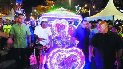 阿末扎希（中）坐著三轮车进入在马六甲古城门前举办的全国圣诞节庆典现场。