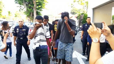 5名男被告在押往法庭面控期间，拉起T恤衣领遮脸。