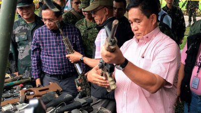 菲律宾国防部长洛伦扎纳（中）在国家安全顾问陪同下，在马拉维市一处军营，视察从武装分子藏身处缉获的逾100把枪支和弹药。