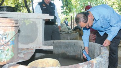 马汉顺（右）以手电筒照射洋灰水槽里，仔细检查积水处是否有孑孓滋生。