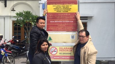 黄顺祥（左起）偕同槟岛市议员卡拉及李俊杰，展示槟岛市政厅张贴的统一停车收费时间的告示贴纸。