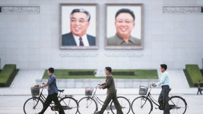 这是在金日成广场的朝鲜民众，推著脚车经过朝鲜已故最高领导人金日成和金正日的画像。
