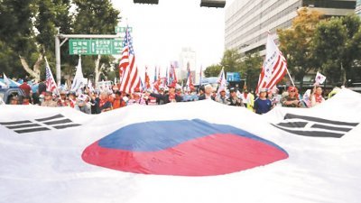 周日是韩战爆发67周年，朝韩各自有活动纪念。图为韩国民众在首尔拉著一面巨幅韩国国旗游行，当中亦有人挥舞美国国旗。