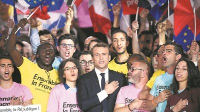中间派候选人马克龙（中）周一在巴黎举行造势活动上，与支持者高唱法国国歌。