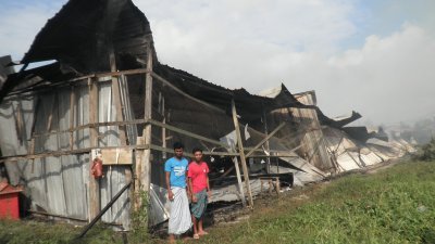 2名外劳站在被火烧毁 的工厂前，一脸无奈。