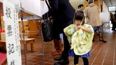 台风带来狂风暴雨，但无阻选民到投票站投票。一名随父亲去投票的小女孩，在父亲填划选票时，解开身上的雨衣。-路透社-