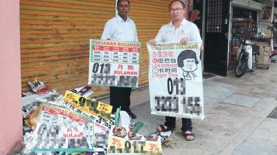 张志坚（右起）与古拉展示有人堆放在其服务中心门前的非法大耳窿宣传放贷横幅。