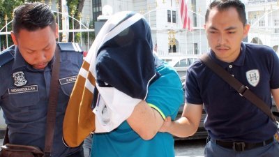 被告罗炳华（中）被关税局官员押往法庭时，全程以衣服遮头。